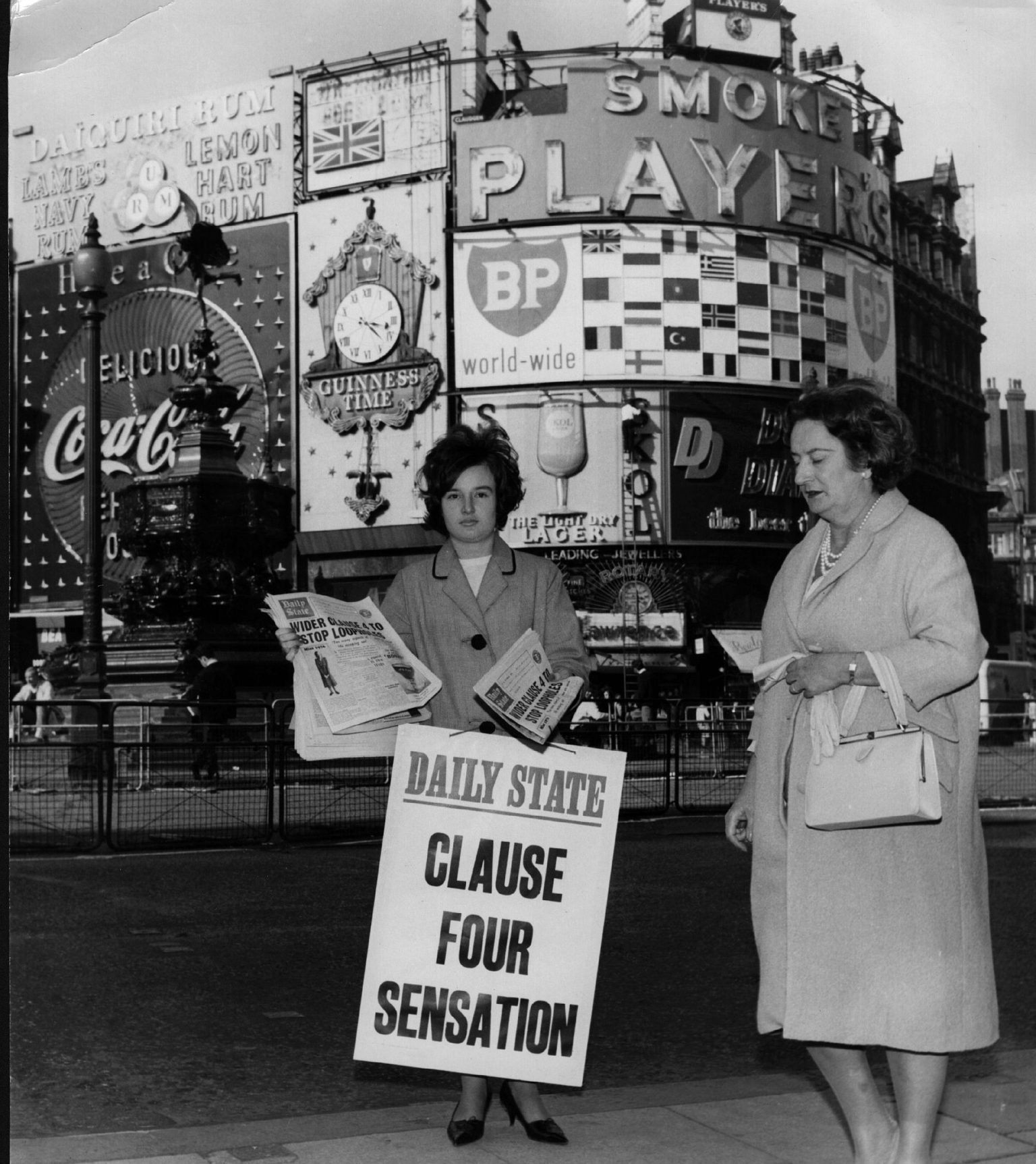A woman at Piccadilly Circus selling a mock newspaper predicting a fully nationalised future, on 30 September 1963.