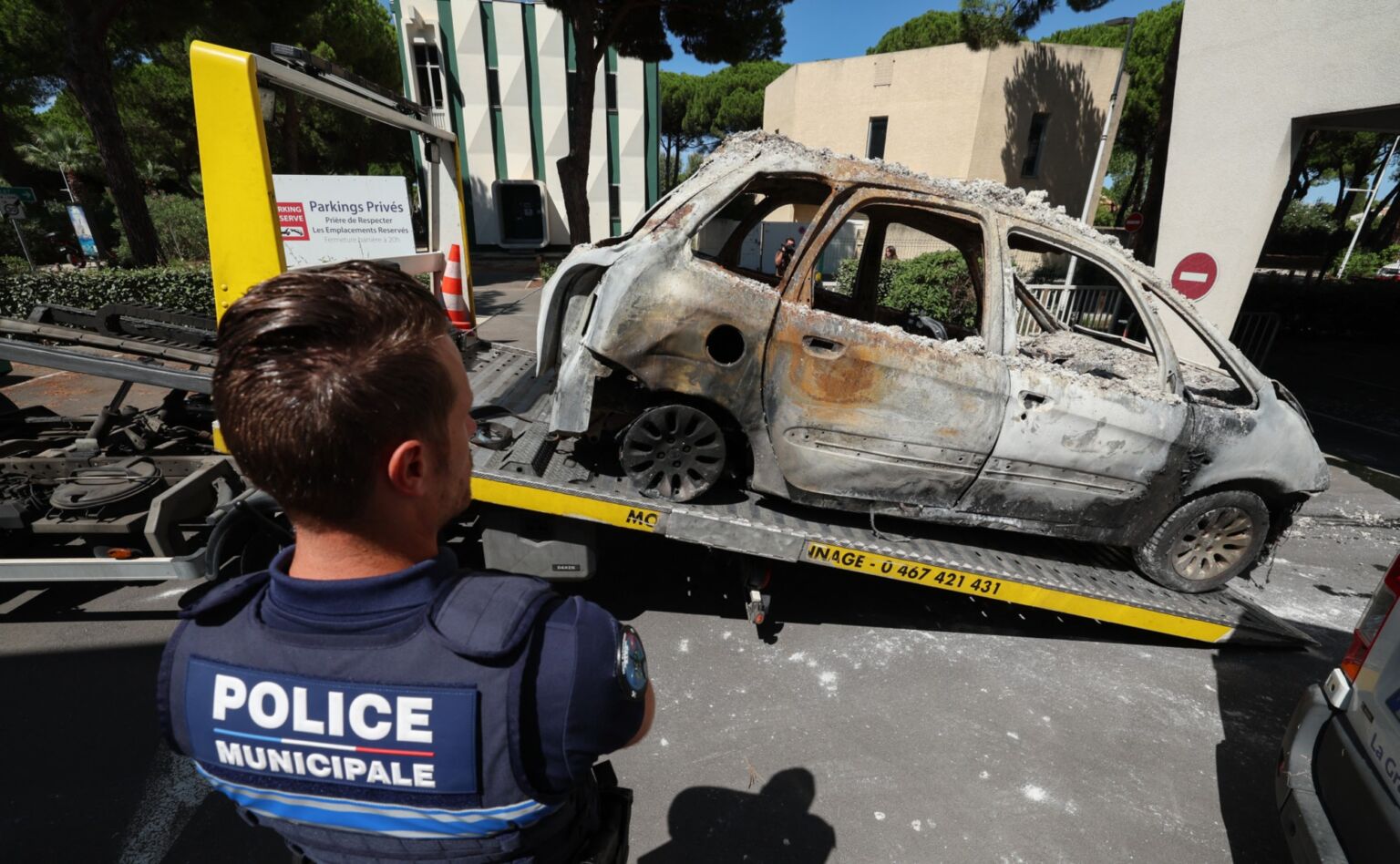 A Police officer stands in front of a car set on fire during the attack on the Beth Yaacov synagogue in Montpellier, France,  26 August 2024.