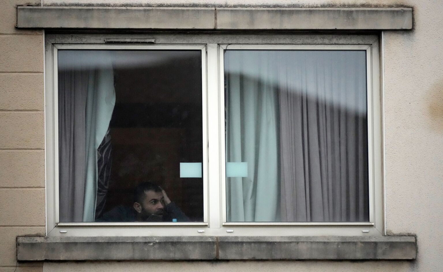 A man looks out of the window at the Suites Hotel in Knowsley, Merseyside, the morning after the riots, 11 February 2023.